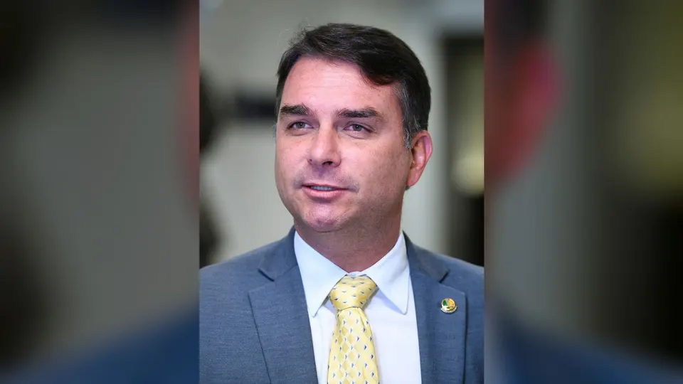Senador Flávio Bolsonaro, de terno e gravata, falando durante entrevista